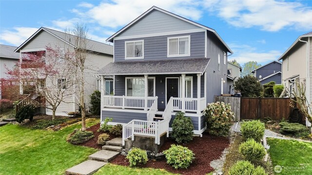 view of front of home featuring a porch, a shingled roof, fence, and a front lawn