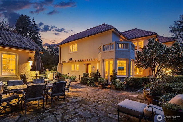 180 Lake Washington Blvd E, Seattle, WA 98112 - back of property at dusk with a tile roof, a patio, outdoor dining area, stucco siding, and a balcony