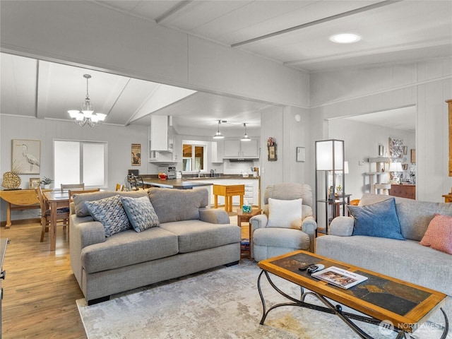 living area featuring lofted ceiling with beams, light wood finished floors, and a notable chandelier