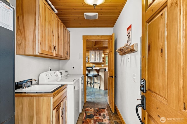 laundry area featuring washing machine and clothes dryer, stone finish floor, cabinet space, wood ceiling, and a sink