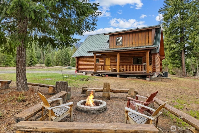 back of house with log siding, a porch, central AC, an outdoor fire pit, and metal roof