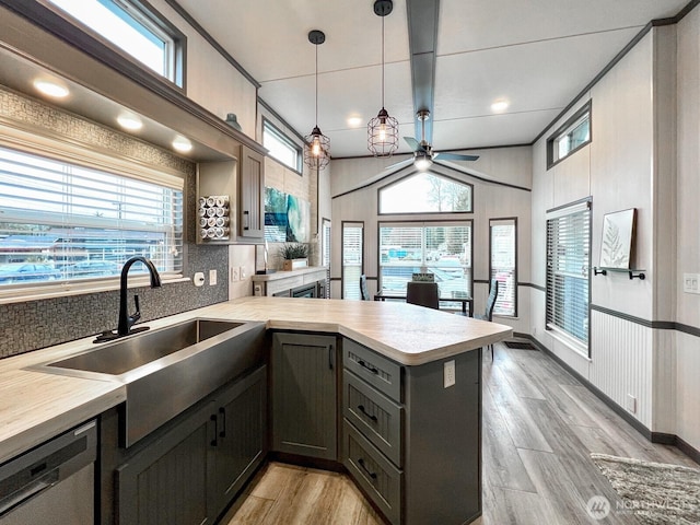 kitchen with stainless steel dishwasher, a peninsula, a ceiling fan, light countertops, and a sink