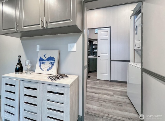 kitchen with light countertops, gray cabinetry, stacked washer / dryer, and light wood finished floors