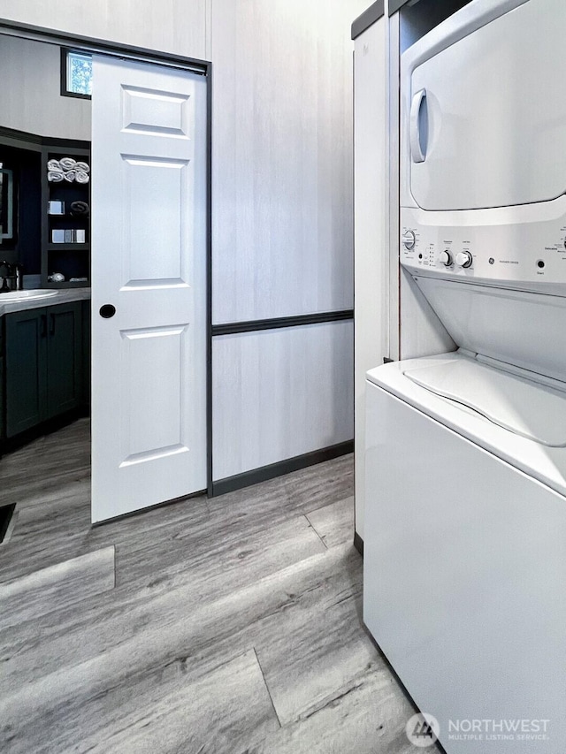 laundry room with a sink, stacked washing maching and dryer, and light wood-style floors