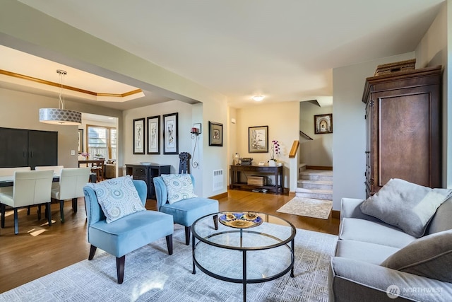 living room featuring stairway, visible vents, baseboards, and wood finished floors