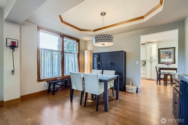 dining space featuring a tray ceiling, crown molding, light wood finished floors, and baseboards