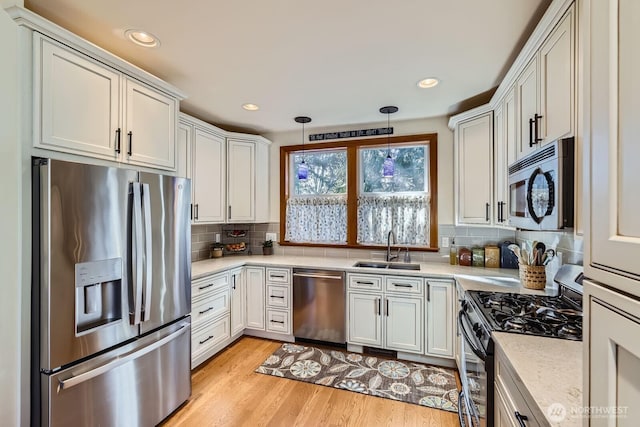 kitchen with appliances with stainless steel finishes, light wood-style flooring, decorative backsplash, pendant lighting, and a sink