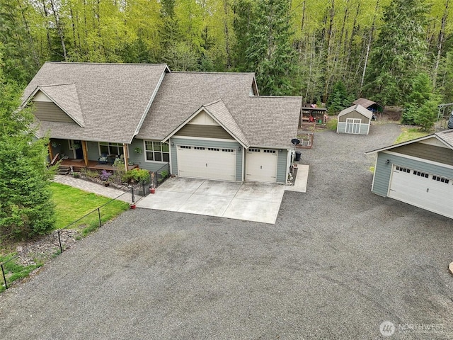 view of front of house with an attached garage, driveway, a wooded view, and a shingled roof