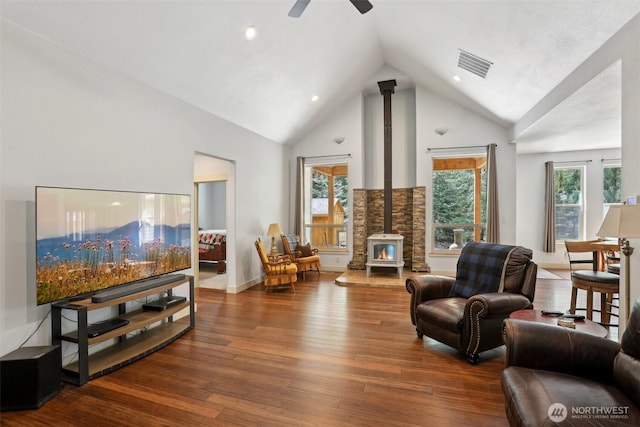 living room featuring high vaulted ceiling, a ceiling fan, wood finished floors, a wood stove, and visible vents