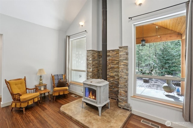 living area featuring vaulted ceiling, a healthy amount of sunlight, a wood stove, and visible vents