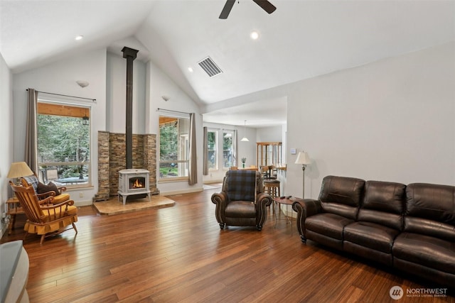 living room featuring high vaulted ceiling, ceiling fan, a wealth of natural light, a wood stove, and visible vents