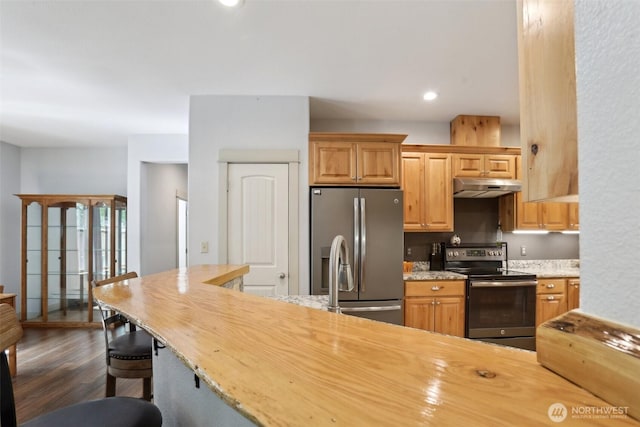 kitchen with light stone counters, a kitchen breakfast bar, stainless steel appliances, under cabinet range hood, and dark wood-style floors