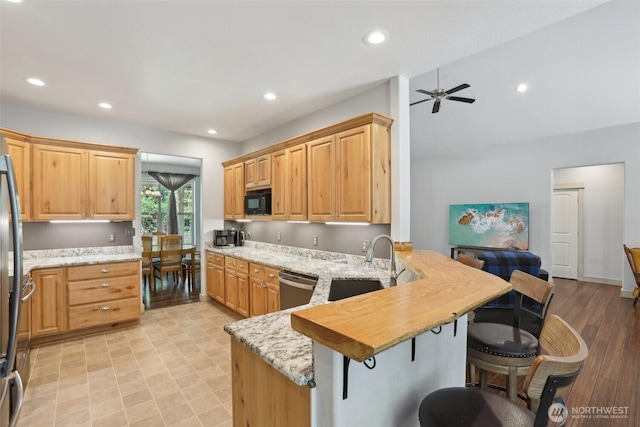 kitchen with a peninsula, stainless steel dishwasher, a sink, a ceiling fan, and a breakfast bar