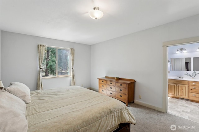 bedroom with baseboards, ensuite bath, light colored carpet, and a sink