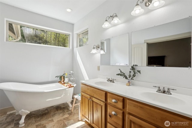 full bath with stone finish floor, a freestanding tub, a sink, and double vanity