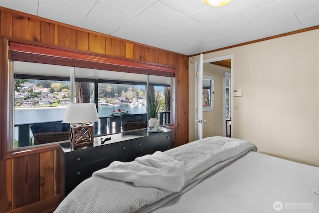 bedroom with crown molding, wood walls, and a water view