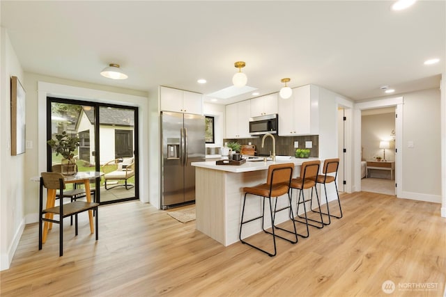 kitchen with a kitchen breakfast bar, a peninsula, white cabinets, appliances with stainless steel finishes, and light wood finished floors