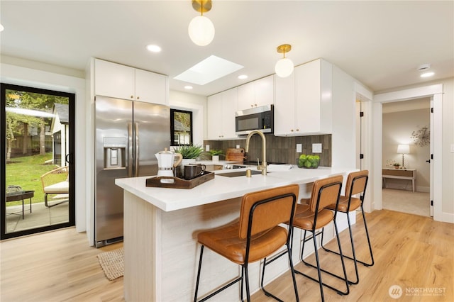 kitchen featuring a kitchen bar, tasteful backsplash, a skylight, appliances with stainless steel finishes, and a sink