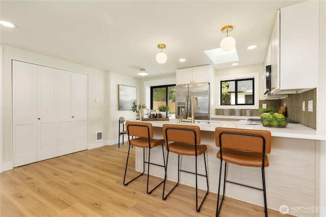 kitchen with stainless steel fridge with ice dispenser, a peninsula, light countertops, visible vents, and a skylight