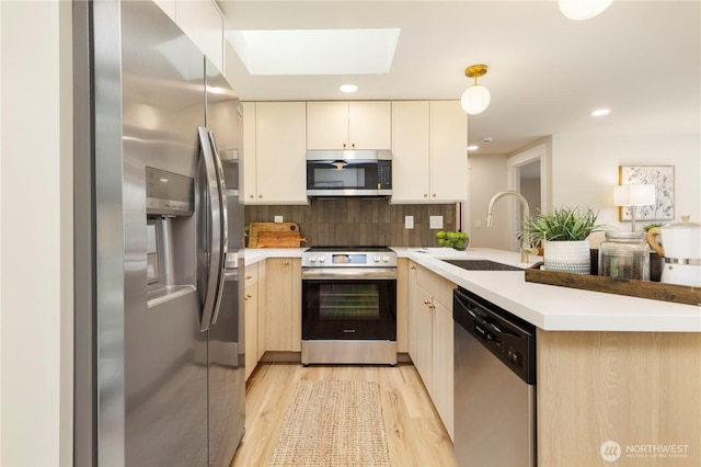 kitchen with tasteful backsplash, a peninsula, light countertops, appliances with stainless steel finishes, and a sink