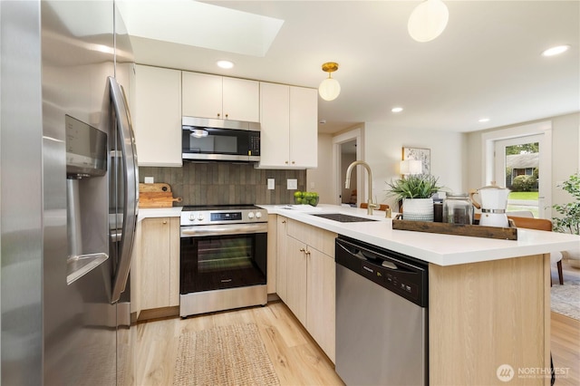 kitchen with a sink, light countertops, a peninsula, stainless steel appliances, and a skylight