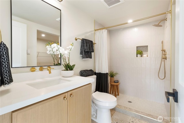 full bath with toilet, tiled shower, vanity, and visible vents