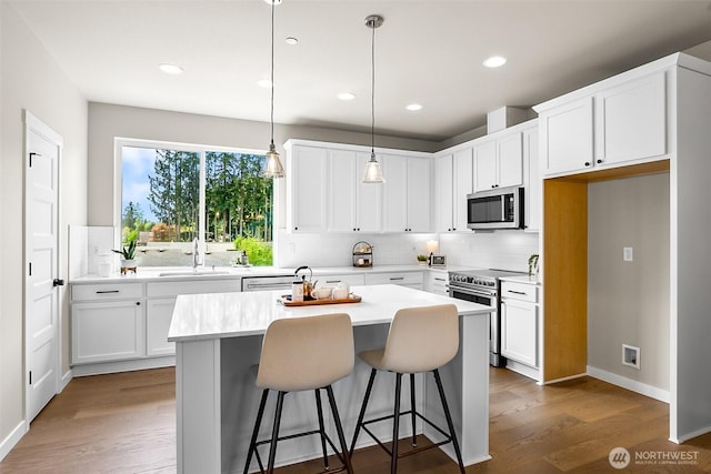 kitchen featuring white cabinets, appliances with stainless steel finishes, a sink, a center island, and decorative backsplash