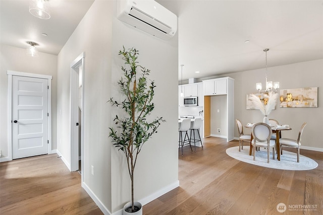 interior space featuring light wood-style floors, baseboards, a wall unit AC, and a notable chandelier