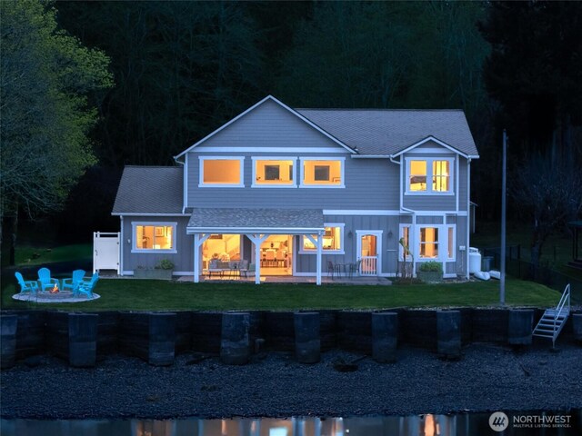 back of house at night with a yard, a fire pit, and a patio