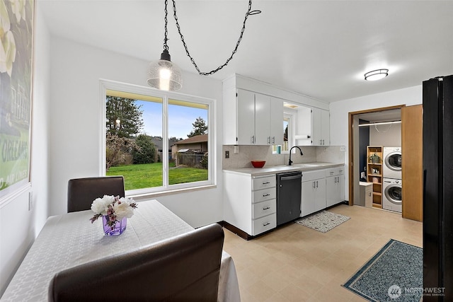 kitchen featuring white cabinets, dishwasher, a sink, light countertops, and stacked washer / drying machine