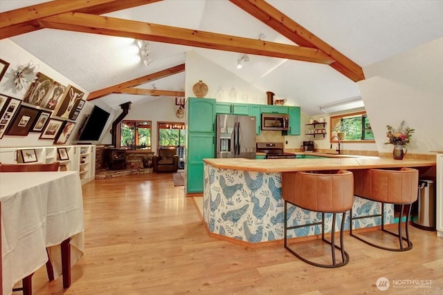 kitchen featuring green cabinets, a peninsula, light wood-style floors, a breakfast bar area, and appliances with stainless steel finishes