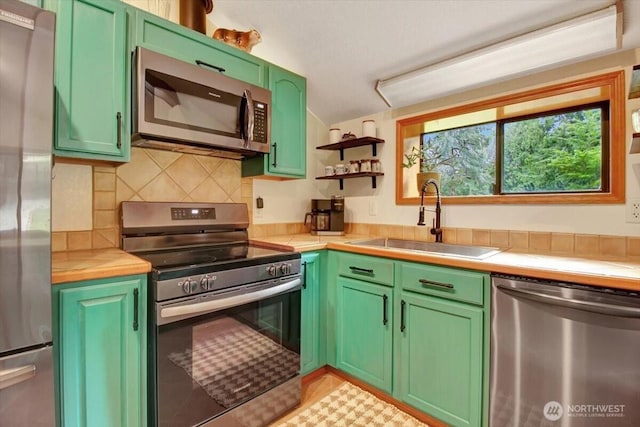 kitchen featuring open shelves, a sink, appliances with stainless steel finishes, green cabinets, and decorative backsplash