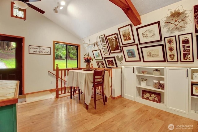 dining space with light wood-style floors, ceiling fan, and lofted ceiling with beams