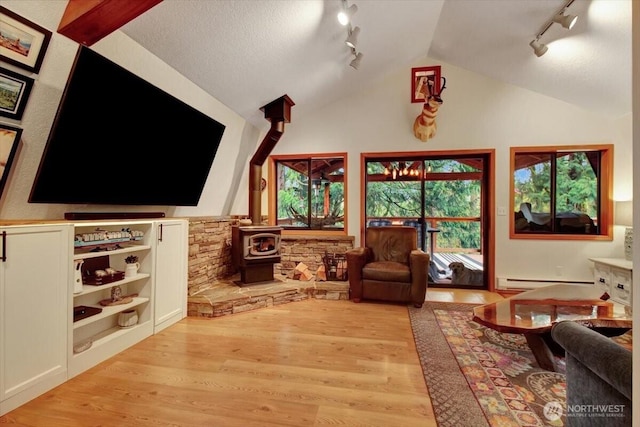 living area with a wood stove, light wood-type flooring, baseboard heating, and lofted ceiling