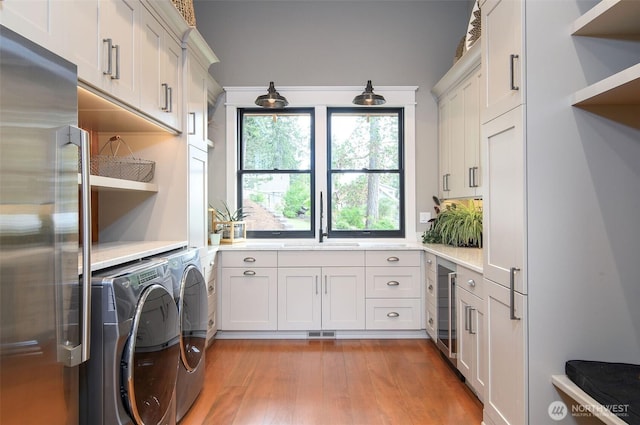laundry area featuring washing machine and clothes dryer, light wood-style floors, cabinet space, and beverage cooler