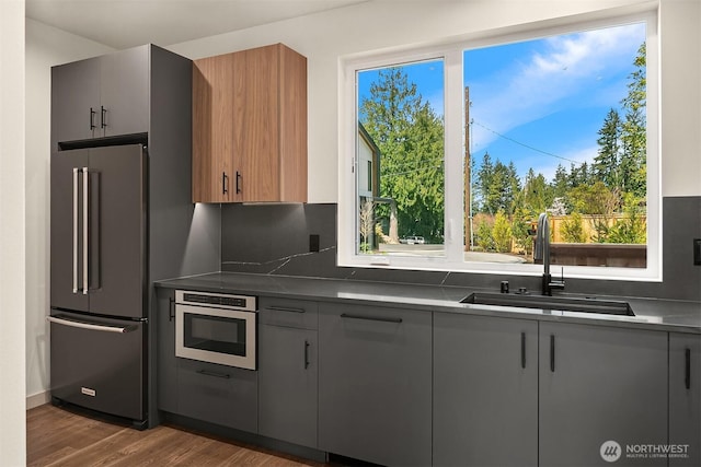 kitchen with dark wood finished floors, dark countertops, high end refrigerator, a sink, and stainless steel oven