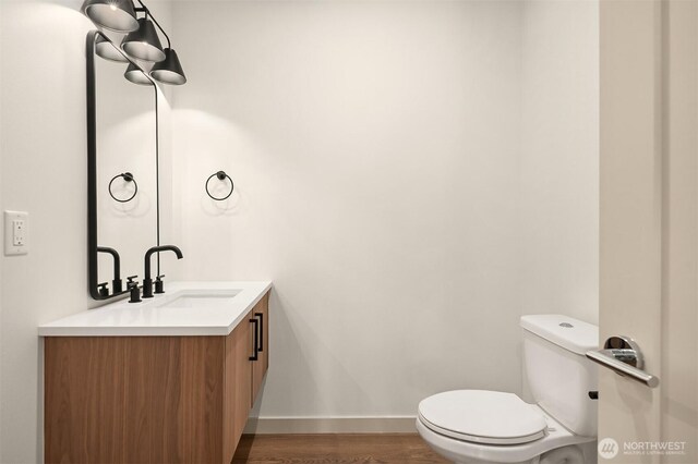 bathroom with toilet, wood finished floors, vanity, and baseboards
