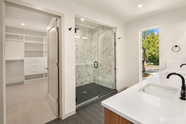 bathroom featuring a walk in closet, recessed lighting, a marble finish shower, and a sink
