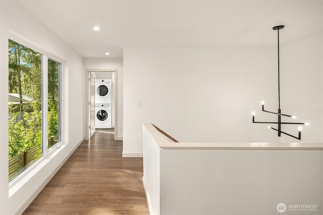hallway featuring stacked washer / drying machine, recessed lighting, an upstairs landing, baseboards, and wood finished floors