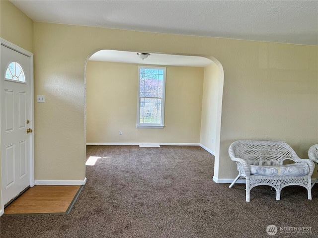 foyer entrance with carpet flooring, baseboards, and arched walkways