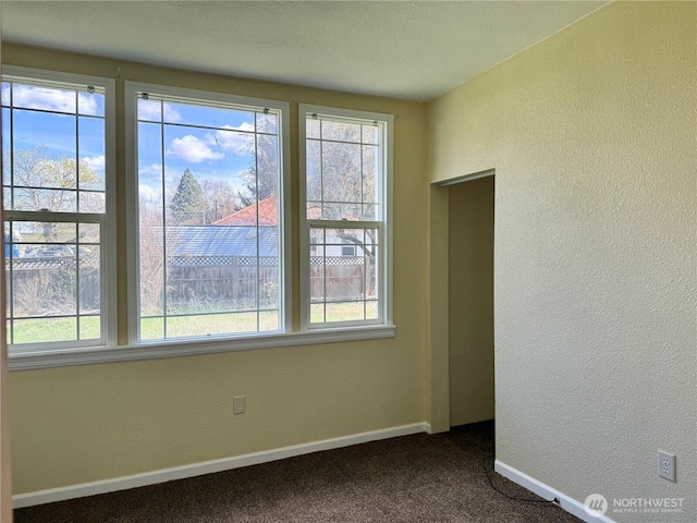 empty room with a textured wall, baseboards, and dark carpet