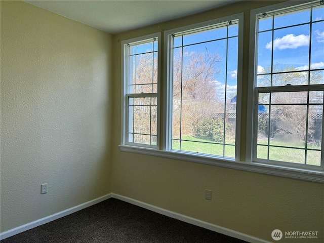 unfurnished room featuring a textured wall, baseboards, and dark colored carpet
