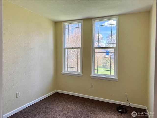 spare room featuring baseboards, dark colored carpet, a textured wall, and a textured ceiling