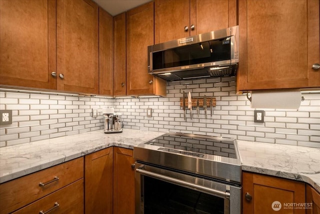 3435 California Ave SW Unit 405, Seattle, WA 98116 - kitchen featuring backsplash, brown cabinetry, light stone counters, and stainless steel appliances