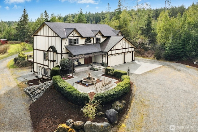 tudor home featuring a garage, board and batten siding, a view of trees, concrete driveway, and roof with shingles