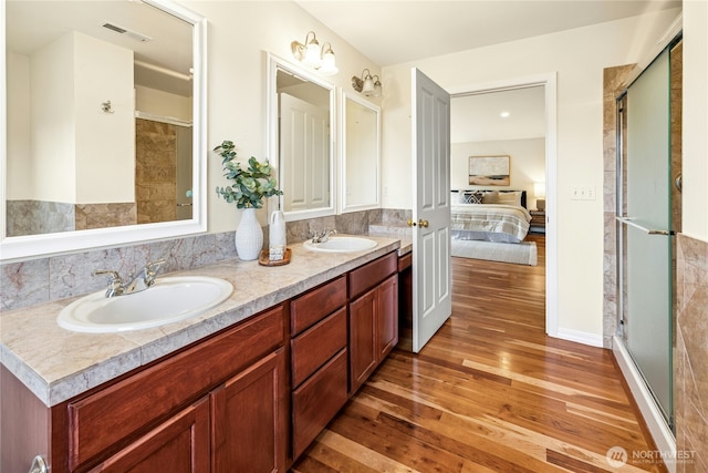ensuite bathroom featuring a shower stall, visible vents, a sink, and wood finished floors