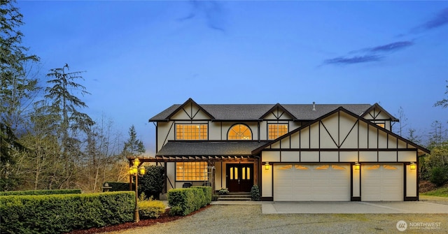 tudor home featuring roof with shingles, driveway, stucco siding, and an attached garage