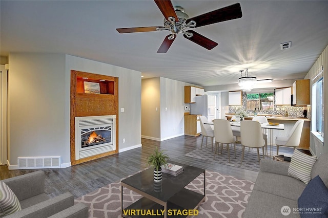 living area with a glass covered fireplace, visible vents, and dark wood-style floors