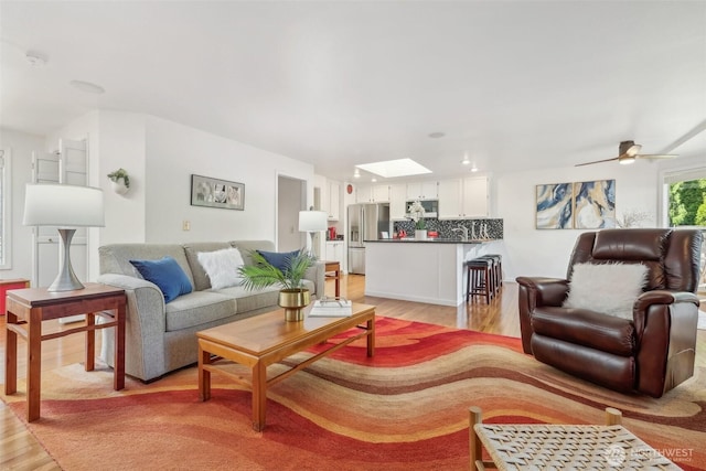 living area featuring ceiling fan, light wood finished floors, and a skylight