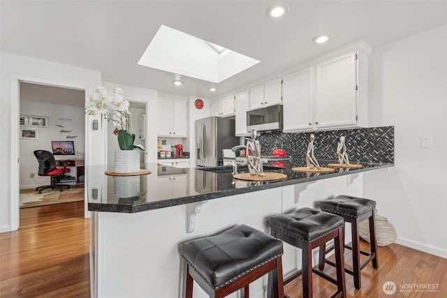 kitchen with white cabinetry, wood finished floors, a peninsula, stainless steel fridge, and a skylight